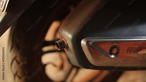 Old exhaust and muffler on motorbike in golden light. Scooter tire, license plate and exhaust system closeup. Motorcycle parts with dirt and rust. Zoom in.