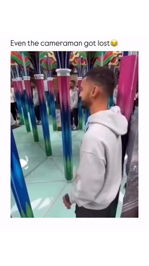 FUNNY MEMES on Instagram: "This video captures a playful and chaotic moment inside a brightly lit mirror maze, likely at an amusement park or attraction. The main subject is a young man with a beard and a fade haircut, wearing a light gray hooded sweatshirt and dark pants. The environment is disorienting, featuring colorful, vertical pillars—primarily magenta, blue, and green—with mirrored walls and a mirrored floor, creating an infinite series of reflections of the man and the columns. At the b