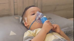 Little 2 years old boy does therapeutic inhalation using a nebulizer.Child takes a breath through inhaler mask at home.Kid treats inflammation of airways via nebulizer for preventing asthma and cough.
