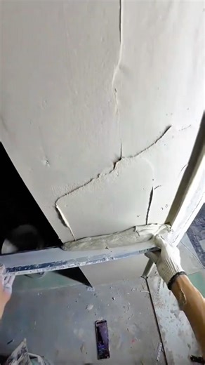 Ceiling plastering worker using a long level float to smooth fresh cement on an overhead surface