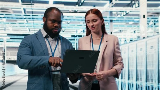 Engineering team in server hub working together with laptop to do maintenance tasks on machines. Teamworking colleagues in modern high tech data center configuring server settings, camera B