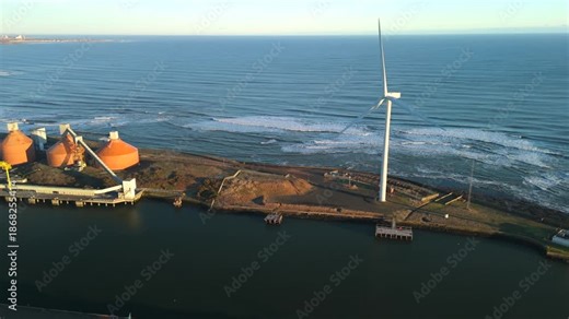 Blyth Northumberland UK: 31st Dec 2025: Drone aerial view of Port of Blyth with docks and industrial buildings along the water. Waves crash along the shore, and a wind turbine stands tall