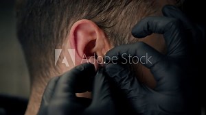 Tattoo piercing studio - a woman makes an ear piercing to a man to a guy