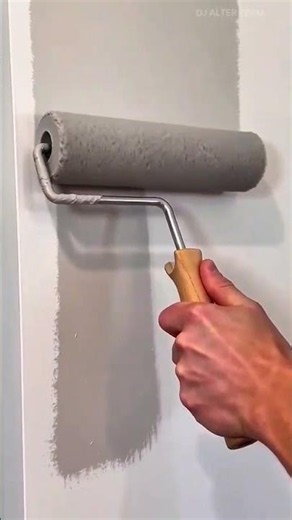 applying grey paint to a vertical wall surface using a paint roller for an even and smooth coverage