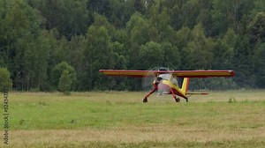 small bright yellow-red civilian small aircraft accelerates across field and is ready to take off. propeller plane on runway with trees in background is about to fly.