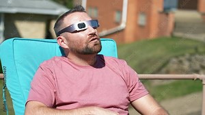 A slow motion view of a man eating popcorn while looking at a total solar eclipse while wearing protective eclipse sunglasses.