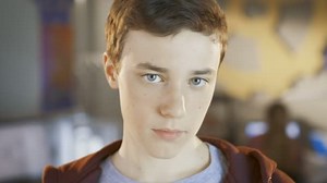 Rapaz inteligente olha e sorri para a câmara. Na aula de Ciência da Computação de fundo.