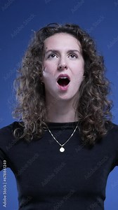 Woman doing epiphany head explosion with hands standing on blue backdrop. Close-up person makes mind blowing gesture in video