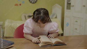 A little girl with long hair is reading a book in her room. Cute little girl reading a book, turning the page, learning, working, studying, reading a book.
