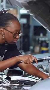Vertical video Licensed engineer in garage using torque wrench to tighten bolts inside opened up vehicle, preparing to change oil. Auto repair shop professional doing checkup on car to prevent