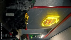 vertical video At a service station a neon sign in the shape of an oil tank hangs on the wall yellow and red light