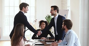 Two happy successful business partners manager and client wear suit shake hand at board diverse group meeting table express respect gratitude make acquisition deal partnership trust agreement concept