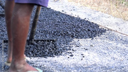 Indian workers use tools to spread hot asphalt on ground for road repair . Bitumen road construction work site.