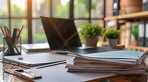 A messy desk with a laptop, papers, and office supplies. The image conveys a sense of busy work.