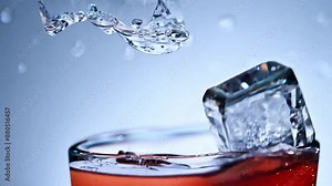 Ice cubes falling in slow motion into a cola drink in a glass.