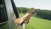 Unrecognizable young woman puts her bare feet out of the car window...