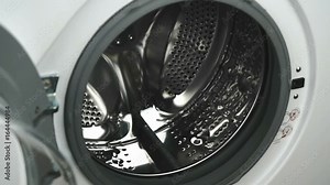 Person's hand opens the door of the washing machine. White washing machine with front-loading laundry, door of laundry load with clear glass for monitoring operation. Close-up