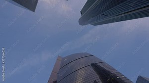 Skyscrapers, bottom view with rotation. The movement of the frame from the bottom up and in the opposite direction. Financial district of the city. Clear blue sky and white clouds. Daytime