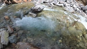 Traveler explores a mountain river. It moves up the river. He has in his hands an action camera with a stabilizer.