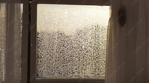 Close-up view of beautiful texture on glass with frozen pattern on sunny winter day. Close-up of frosty natural pattern on window glass on background of bright sunlight. Shooting in slow motion.