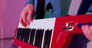 Musician with red keytar in hands playing in band on concert in club, hands close-up. Man dances to the rhythm of music. Musical performance, play in group, enjoying working artist on stage concept.