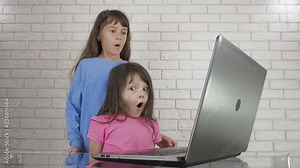 Frightening children at the computer. Little girls are shocked by what they see in the laptop monitor.