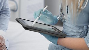 A gloved healthcare professional is using a tablet to review patient information during a consultation, showcasing the advancements of modern medical technology in todays healthcare