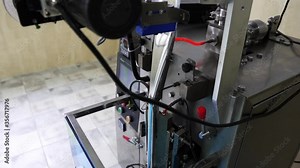 The working process of the metal technical device at the enterprise for packing in plastic sachets foodstuff, the heated mechanical metal press creates packing, a side view, a close-up