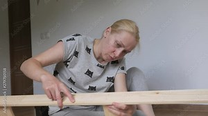 Woman housewife sitting in the room on the floor, collects wooden rack, bought in the store. Assembly of furniture.