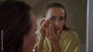 Woman looking in a mirror, focusing on the pimples on her face. She looks concerned and worried about her skin