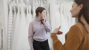 We see the conversation between 2 brunette girls on video. They are in a wedding salon. One of them is a future bride and another is a consultant in the store,she help to choose the dress for client.