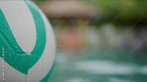 A Green White Beach Ball Floats in the Pool, Close-up. A Rubber children's ball floats past a camera in the pool in the background stands an attractive tanned man with a beautiful torso. slow motion
