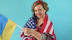 Adult pin-up woman in plaid shirt with USA flag waving Ukrainian flag on isolated blue background. Slow motion portrait. Forty-year-old American woman smiling