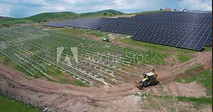 Construction workers installing solar panels on expansive farm. Aerial view of construction workers and machinery installing solar panels on a large solar farm, showcasing sustainable energy