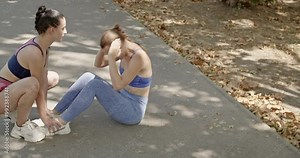 Two fit young women motivate and support each other while exercising in the park.
