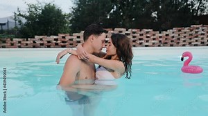Loving young couple enjoying romantic date in swimming pool. Lovers hugs stay close to each other in backyard pool, touch with their noses