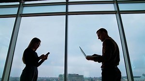 Young workers use laptop and phone in office. Business people changing their gadgets on the sky background through the windows. Business concept.