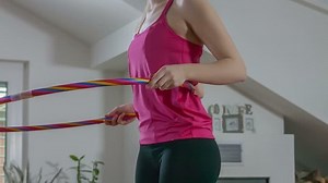 This young woman is doing a Hula-Hoop workout in a living room at her house. Close-up shot.