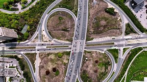 Drone view of a highway interchange with a condo amidst greenery, showcasing urban traffic and residential contrast.