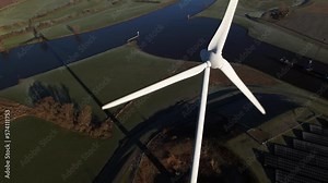 Closeup aerial rotating pan around single windmill revealing solar panel park and sustainable industry in The Netherlands where Dutch river IJssel and Twentekanaal meet. Circular economy concept.