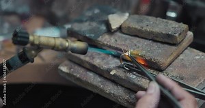 jeweler solders a silver blank with a gas burner in the process of creating a jewelry ring
