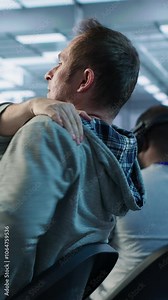 Fatigued admin stretching at work in server room to relieve muscle cramps while analyzing data on monitor. Tired man in data center relaxing body after overworking, camera A