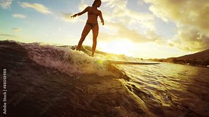 Beautiful Young Woman Surfs a Longboard on an Ocean Wave in Slow MOtionThrough a Golden Sunset with Lens Flares in Hawaii