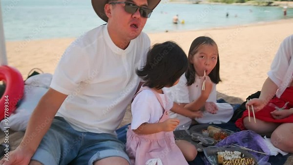 Family picnic on the beach with kids and food from delivery, mom with kids sits on a picnic mat on the sand near the sea.