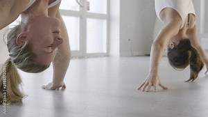 Two women hang upside down in an aerial yoga stretch position