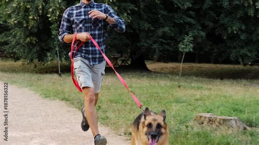 A young man runs along a park path with a German Shepherd keeping pace beside him. The footage shows active outdoor exercise and the dynamic bond between a person and a dog. Canicross concept