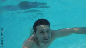 A man swims underwater in a pool. A young active man dives and swims underwater in an outdoor pool