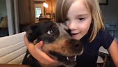 A cute young girl holds her dog close while on a video chat at home