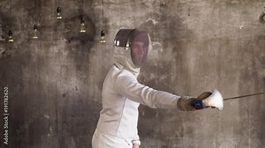 Male professional swordsman is fully equiped improving his moves with a sword. Training alone in a studio.