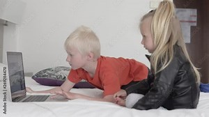 Children watch a cartoon on the computer. Brother and sister sit on the bed in the hotel and watch a cartoon Stock Video
